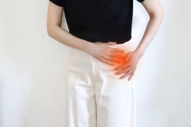 赤ちゃんを抱っこしたまま立ち上がり、脚の付け根の痛みを気にする産後の女性